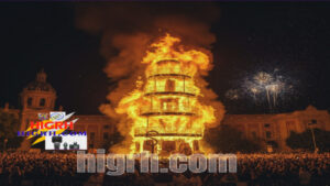 Crowds gathered in Valencia during the Fallas Festival in Valencia watching a large monument burning with fireworks in the background.