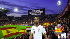 A soccer player on the pitch with a large stadium screen displaying a warning against Islamophobic and xenophobic chants during a match.