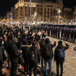 Police officers and a crowd during a nighttime demonstration in Plaça de Catalunya, Barcelona.