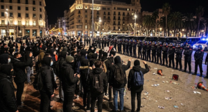 Police officers and a crowd during a nighttime demonstration in Plaça de Catalunya, Barcelona.
